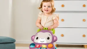 Imagem de bebê sorridente brincando com brinquedo infantil de formato de urso, leão e engrenagens coloridas em sala clara, ao lado de estante branca com portas.