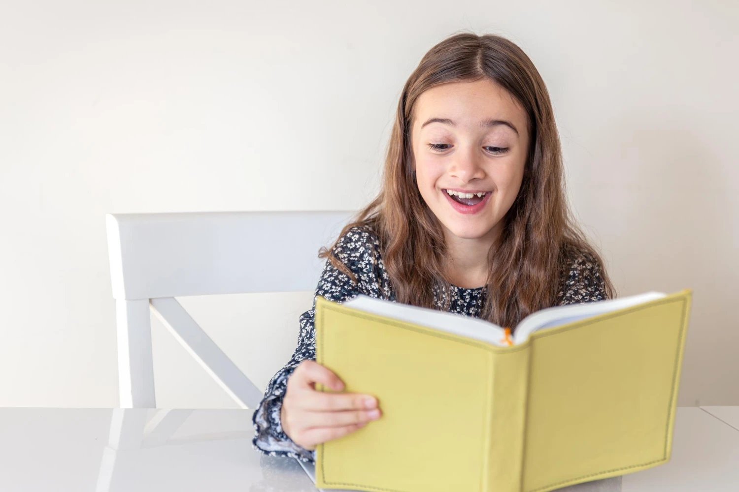 menina sorridente lendo livro amarelo na mesa